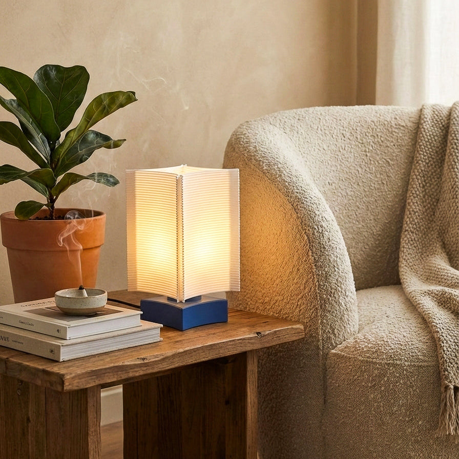 Lamp on a wooden side table next to a plant and a cozy sofa in a living room.
